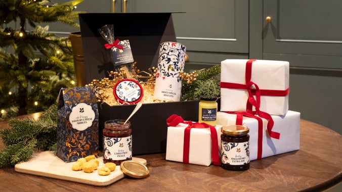 A basket and several parcels alongside Christmas treats including a jar of chutney and biscuits.
